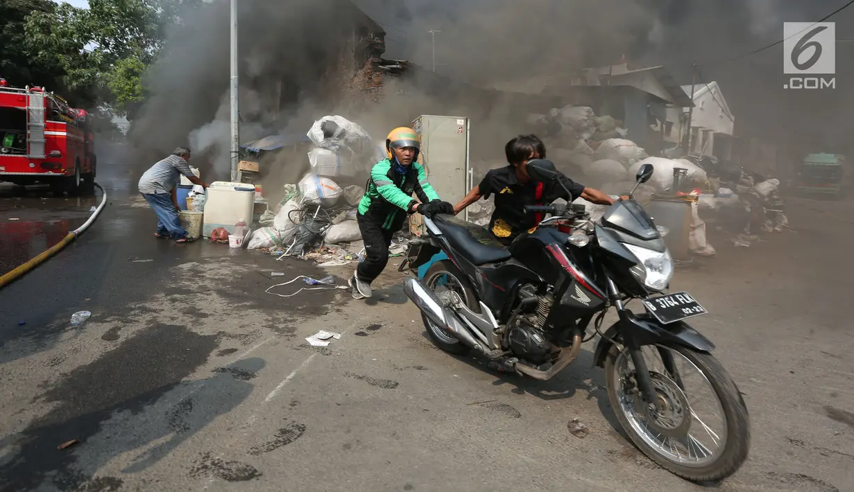 Pengemudi ojek online mendorong sepeda motor saat kebakaran melanda sebuah gudang di Jalan Kampung Bandan, Ancol, Jakarta Utara, Kamis (5/7). (Kapanlagi.com/Budy Santoso)