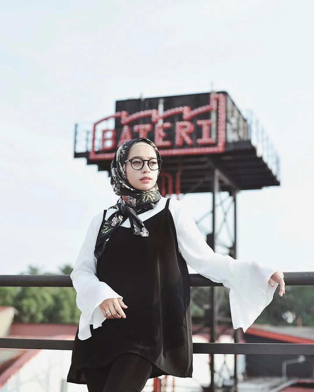 Atasan warna putih dengan aksen ruffle lalu pilih mini dress sebagai luarannya dan celana hitam, buat penampilan hijab kamu trendi. (sumber foto: @joyagh/instagram)