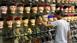 Seorang pria melihat baret militer dan pistol yang dipamerkan di jalan al-Khayyam di Baghdad (13/9). Perang yang berlangsung di Irak membuat para penjahit pakaian biasa kebanjiran orderan membuat seragam militer dan aksesorisnya. (AFP Photo/Sabah Arar)