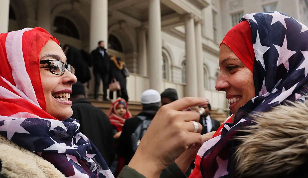 Seorang wanita membantu rekannya memakai kerudung bermotif bendera AS saat perayaan Hari Hijab Sedunia di depan Balai Kota, New York, Rabu (1/2). Hari Hijab Sedunia digagas oleh warga New York bernama Nazma Khan. (Spencer Platt / Getty Images / AFP)