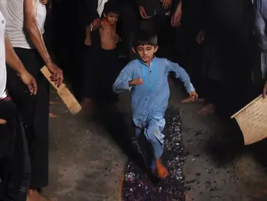 Seorang anak muslim Syiah Pakistan berlari di atas bara api saat peringatan Hari Asyura di Lahore, Rabu (19/9). Hari Asyura diperingati atas kemartiran Imam Hussain, cucu Nabi Muhammad. (ARIF ALI/AFP)