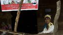 Wanita etnis Kayan duduk di sebelah poster pemilu di desa PanPat, Kayan, Myanmar, Rabu (9/9/2015). Kaum perempuan Suku Kayan ini mengenakan banyak kalung berbentuk cincin di lehernya hingga membuat leher mereka panjang. (AFP PHOTO/Ye Aung THU)
