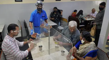 Pramusaji mengenakan pelindung wajah dan masker saat menyajikan makanan kepada pelanggan di restoran yang dibuka kembali usai pelonggaran lockdown di Bangalore, India, Senin (8/6/2020). Untuk keamanan pelanggan, restoran-restoran menyiapkan panel transparan di meja makan. (Manjunath Kiran/AFP)