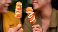Dua orang sedang menunjukkan kuliner kekinian corndog sosis (Sumber: Freepik)