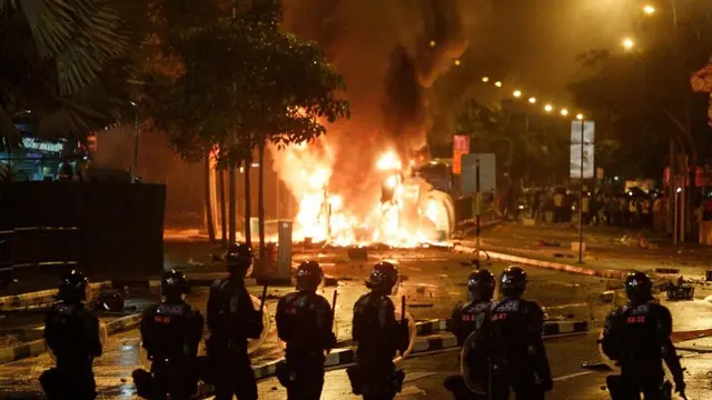 Polisi anti huru hara berjaga saat sebuah kendaraan terbakar setelah terjadi kerusuhan di lingkungan Little India Singapura pada 8 Desember 2013. (AP)