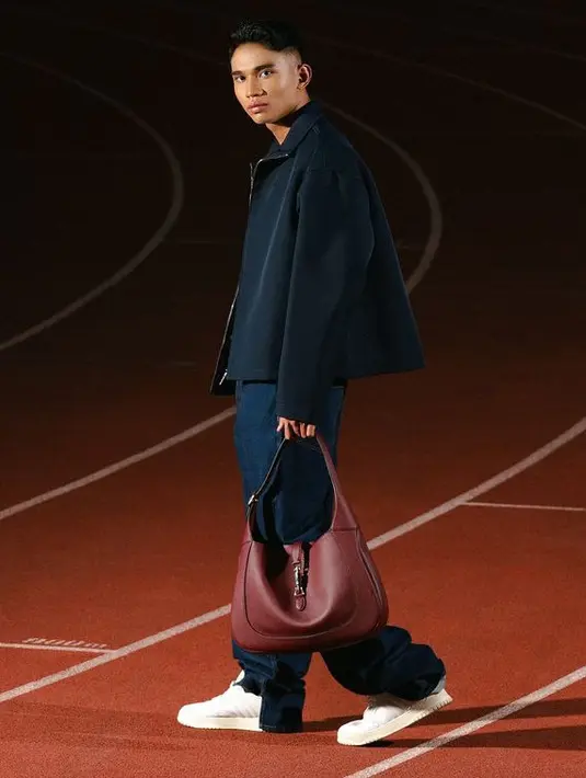 Marselino tampil dengan jaket hitam dipadukan bawahan celana denim sambil membawa handbag maroon. Dipadukan sneakers putihnya. [@kacastuudio]