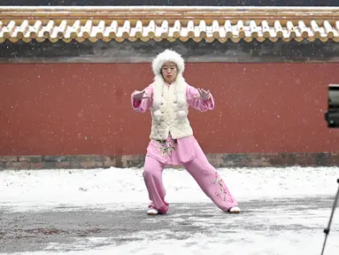 Seorang wanita merekam dirinya melakukan tai chi ketika salju turun di sebuah taman di Beijing (16/12/2019). Salju yang melanda Beijing Senin pagi membuat penerbangan dibatalkan dan rute bus disesuaikan. (AFP Photo/Wang Zhao)