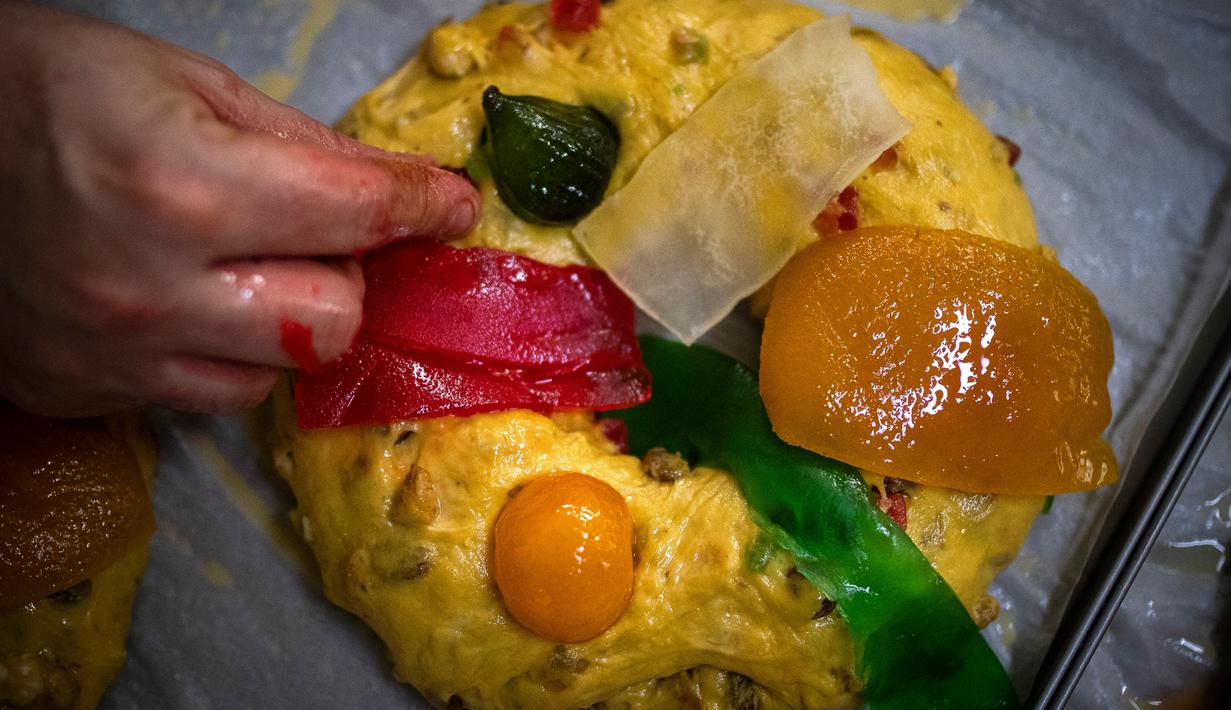 Seorang tukang roti meletakkan buah-buahan mengkristal di atas Bolo Rei atau Kue Raja yang siap untuk dioven di toko roti Padaria da Ne, Amadora, Portugal, 16 Desember 2022. Kue berbentuk cincin ini adalah salah satu sajian khas Natal di Portugal. (CARLOS COSTA/AFP)
