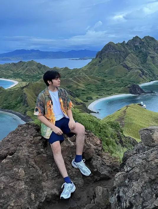 Angga Yunanda tampil dengan kemeja colorfull dengan inner tshirt putihnya saat di Pulau Padar, Labuan Bajo. Ia memadukannya dengan short pants navy dan sneakers New Balance Nya. Credit:  (@angga)