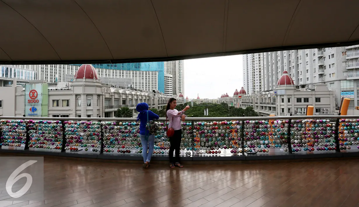 Pengunjung berselfie di depan bola pengharapan di pagar jembatan Eco Skywalk di Mall Central Park, Jakarta, Senin Malam (19/12). Acara tersebut bertujuan untuk kegiatan sosial berbagi kasih dengan anak-anak panti asuhan. (Liputan6.com/Johan Tallo)