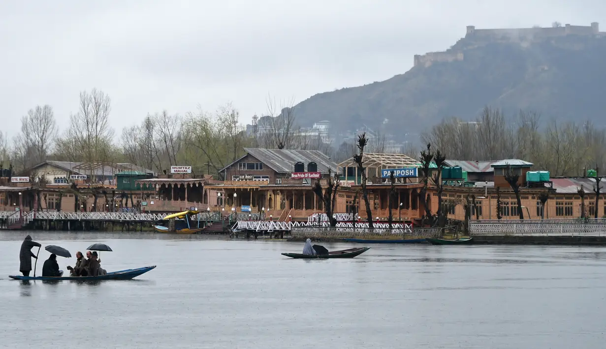 Seorang awak perahu Kashmir mengangkut penumpang saat hujan di Danau Dal di Srinagar (20/3). Danau Dal yang luas dan bening. Diatasnya terhampar gerombolan daun bunga lotus. (AFP Photo/Tauseef Mustafa)