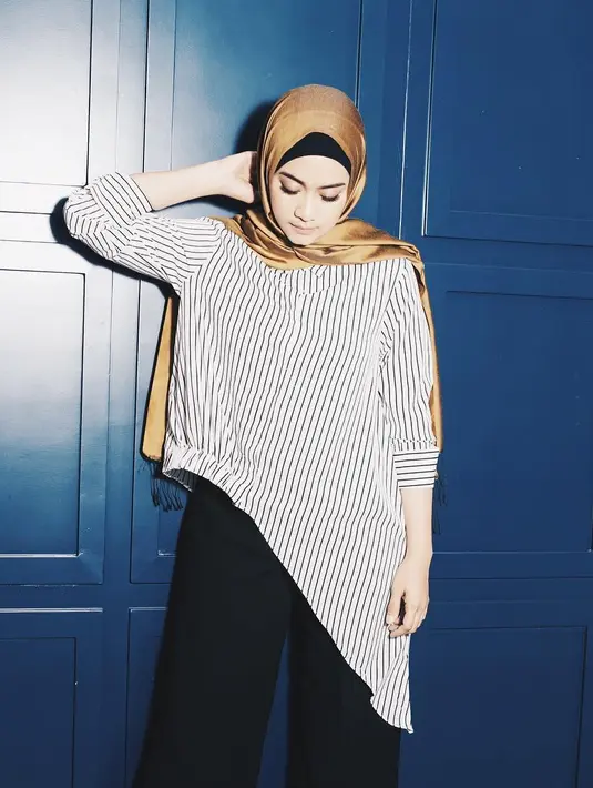 Seperti ini contohnya, Ayudia memadukan celana kulot hitamnya dengan blouse asimetrik bermotif garis-garis dan hijab berwarna gold. Paduan yang serasi untuk dikenakan ibu satu anak ini. (Instagram/ayudiac)