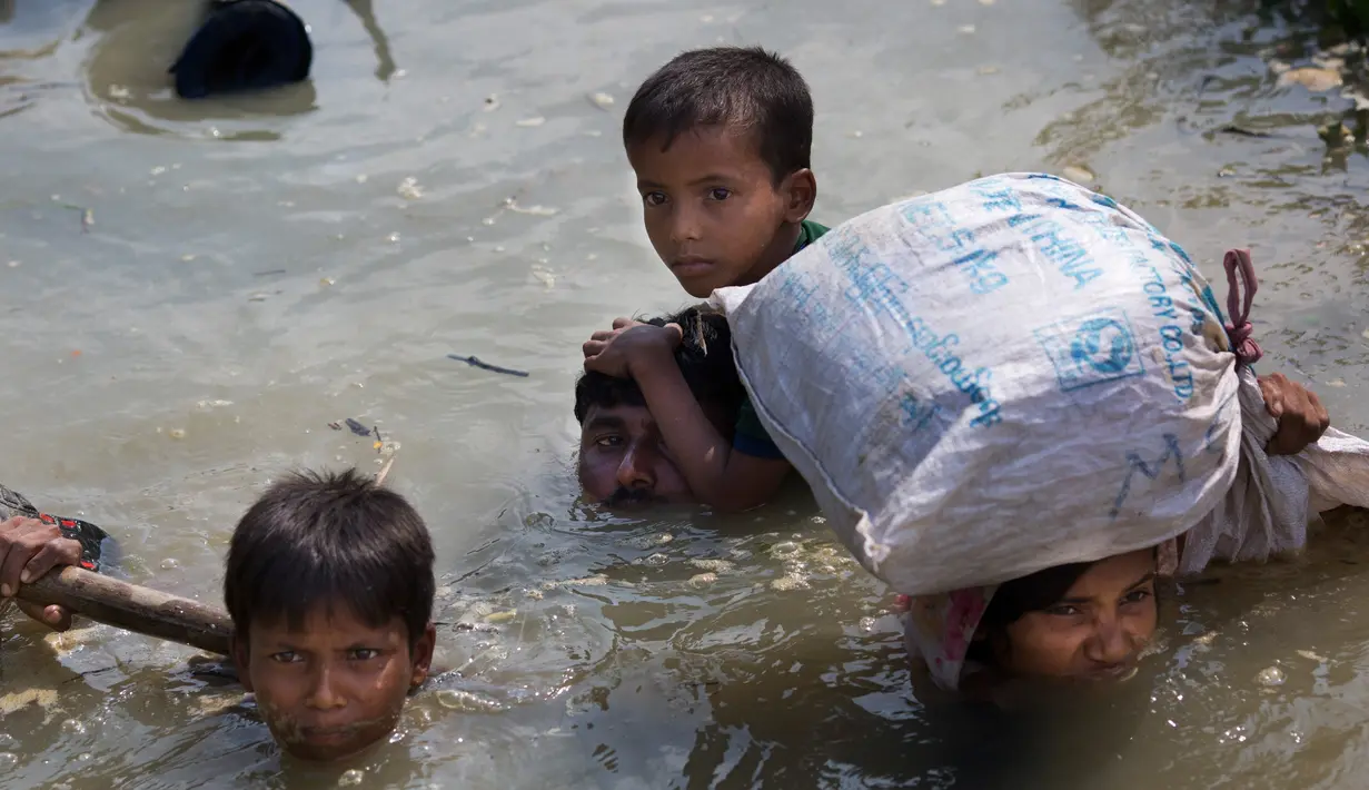 Keluarga minoritas Rohingya membawa anak-anak mereka berjalan menyusuri sungai Naf untuk melarikan diri dari Myanmar menuju perbatasan Bangladesh, di daerah Teknaf Cox Bazar, 5 September 2017. (AP Photo/Bernat Armangue)