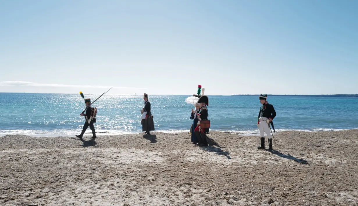 Orang-orang yang mengenakan kostum era Napoleon Bonaparte berjalan di pantai dalam rangka peringatan 200 tahun kematian Napoleon Bonaparte di Saint-Helene, Golfe-Juan, Prancis, 16 Maret 2021. Napoleon memenangkan kebanyakan dari perang dan pertempuran. (Valery HACHE/AFP)