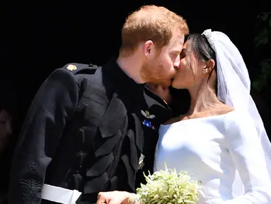 Pangeran Harry mencium istrinya, Meghan Markle di tangga Pintu Barat St George's Chapel, Kastil Windsor, Inggris, Sabtu (19/5). Pangeran Harry dan Meghan Markle telah resmi menikah. (Ben STANSALL/POOL/AFP)
