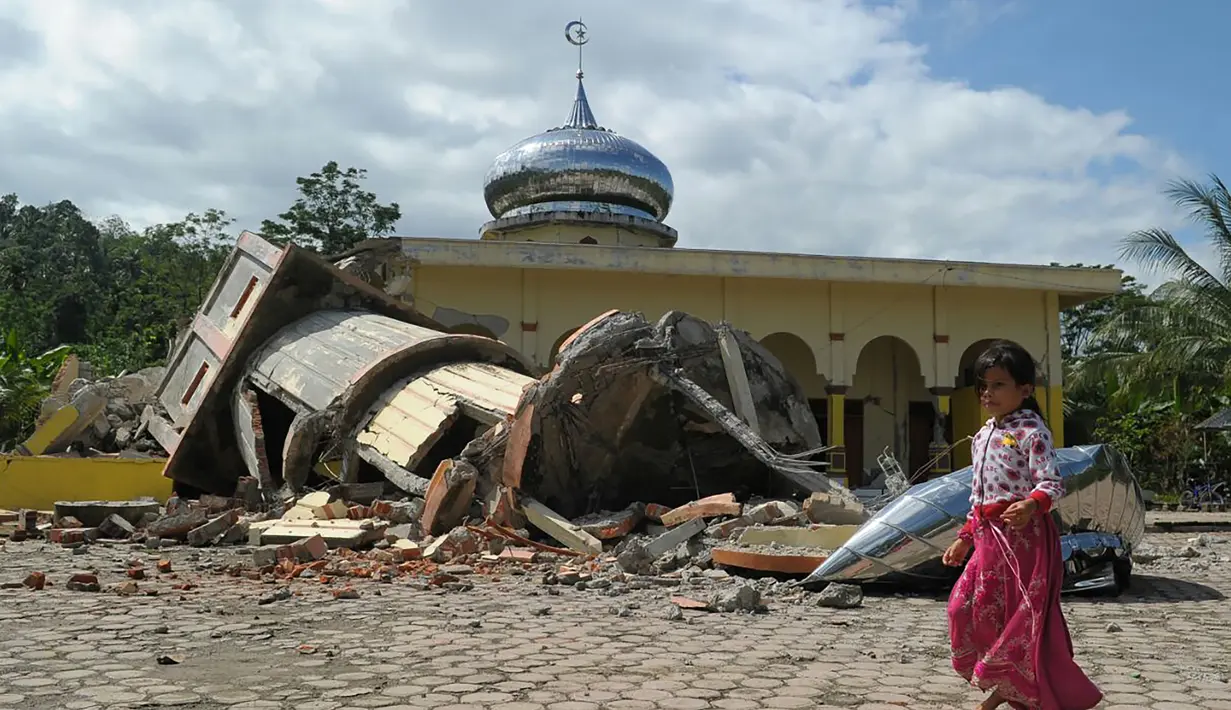Seorang bocah berjalan melewati sebuah masjid yang rusak usai gempa di Pidie Jaya, Aceh, Rabu (7/11). Selain meruntuhkan bangunan, gempa bumi berkuatan 6,4 SR ini telah menelan banyak korban jiwa. (AFP PHOTO / Chaideer Mahyuddin)