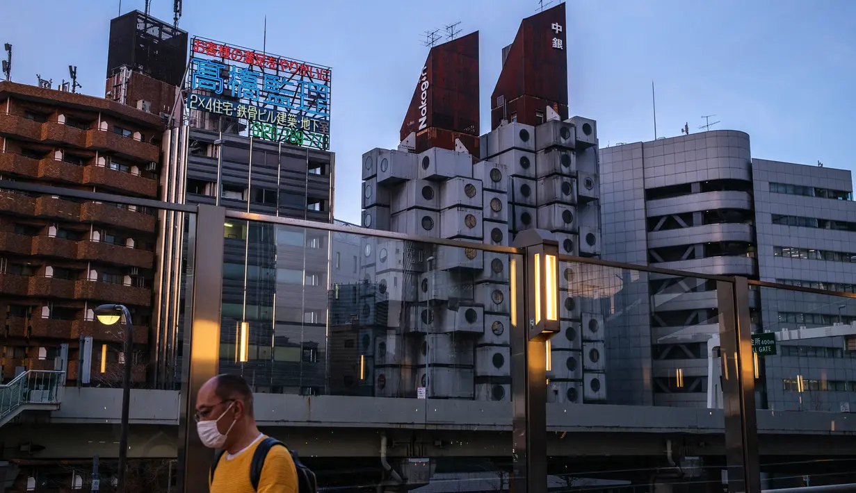 Seorang pria berjalan di sepanjang jembatan sebagai Landmark Nakagin Capsule Tower (tengah kanan), di distrik Ginza Tokyo, 6 April 2022. Menara yang selesai pada tahun 1972 dan dirancang oleh arsitek terkenal Kisho Kurokawa itu adalah sebuah landmark dari gerakan Metabolisme. (Philip FONG/AFP)