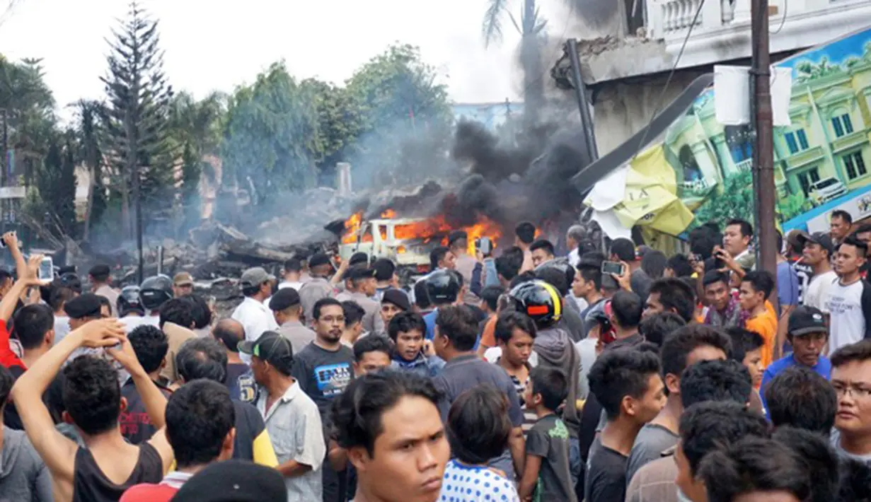 Sejumlah warga berkumpul melihat kecelakaan pesawat Hercules C-130 yang jatuh di kawasan perumahan di Medan, Selasa (30/6/2015). Hercules C-130 milik TNI AU jatuh tidak lama setelah lepas landas. (AFP PHOTO/Muhammad Zulfan Dalimunthe)