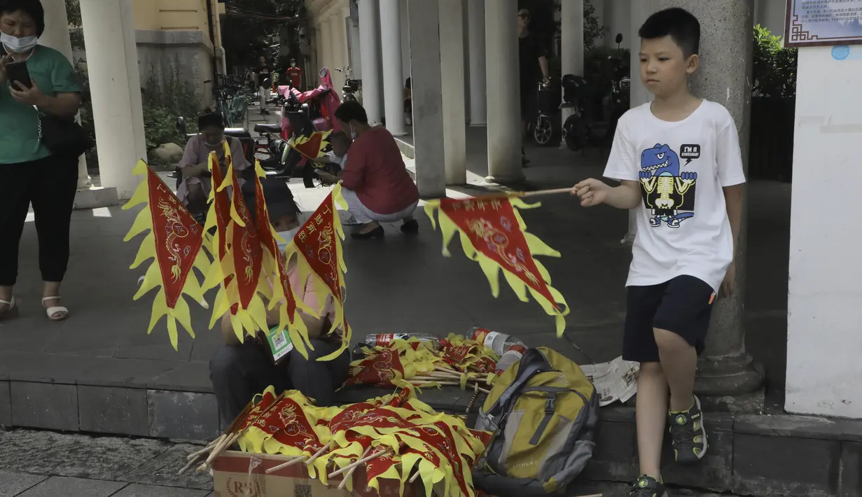 Seorang anak menjual bendera di sepanjang rute perlombaan perahu naga di kawasan bersejarah Teluk Lychee di Guangzhou di Provinsi Guangdong, China selatan, Jumat, 3 Juni 2022. Perlombaan perahu naga kembali digelar di beberapa bagian China untuk pertama kalinya sejak merebaknya pandemi pada akhir 2019, saat pembatasan dicabut bersama dengan penurunan besar  kasus COVID-19. (AP Photo/Caroline Chen)