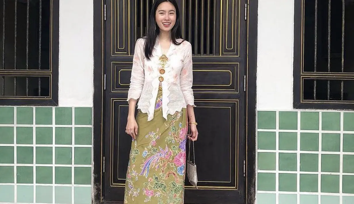 Kebaya putih dengan aksesori bros juga melengkapi penampilannya. Dipadukam kain lilit hijau motif bunga.Credit: @poydtreechada.