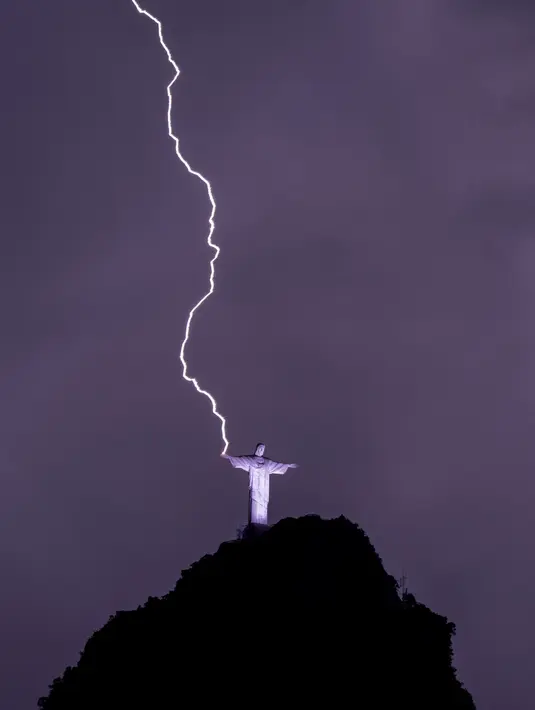 Petir menyambar tangan Christ the Redeemer atau Patung Kristus Penebus di gunung Corcovado di Rio de Janeiro, Brasil, Selasa (21/2/2023). Patung Kristus Penebus merupakan patung Yesus terbesar di dunia  dan menjadi salah satu landmark Rio de Janeiro. (Photo by MAURO PIMENTEL / AFP)