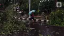 Warga berjalan dekat pohon tumbang yang melintang di sebuah jalan di Kota Tangerang, Banten, Kamis (23/12/2021). Puluhan pohon dan gapura tumbang akibat terjangan angin kencang saat hujan lebat melanda Kota Tangerang. (Liputan6.com/Angga Yuniar)