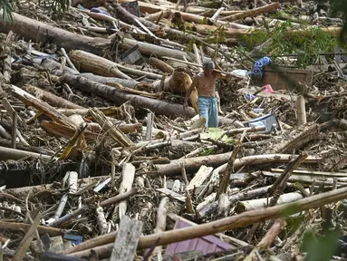 Seorang warga desa terdampak banjir bandang berjalan di antara tumpukan kayu di Desa Tukka, Tapanuli Tengah, Sumatera Utara, pada 2 Desember 2025. Banjir bandang dan tanah longsor yang melanda Kabupaten Tapanuli Tengah sejak 25 November 2025 telah menelan korban. Ada dua desa yang paling parah terdampak, yakni Desa Tukka dan Desa Tanah Bolon. (YT HARIONO/AFP)