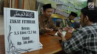 Petugas bersama seorang pria berdoa usai membayarkan zakat fitrah di Masjid Istiqlal, Jakarta, Jumat (23/6). Waktu pembayaran dibuka hingga malam takbiran dengan pembayaran zakat senilai Rp50ribu dan beras 3,5 liter. (Liputan6.com/Helmi Afandi)