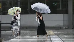 Para perempuan bereaksi saat mereka mengarungi genangan air di persimpangan di tengah hujan di Tokyo, Selasa (20/9/2022). Topan Nanmadol melanda Jepang selama akhir pekan sebelum melemah saat bergerak ke utara. Sejumlah kerusakan baru dilaporkan di Jepang selatan. (AP Photo/Hiro Komae)