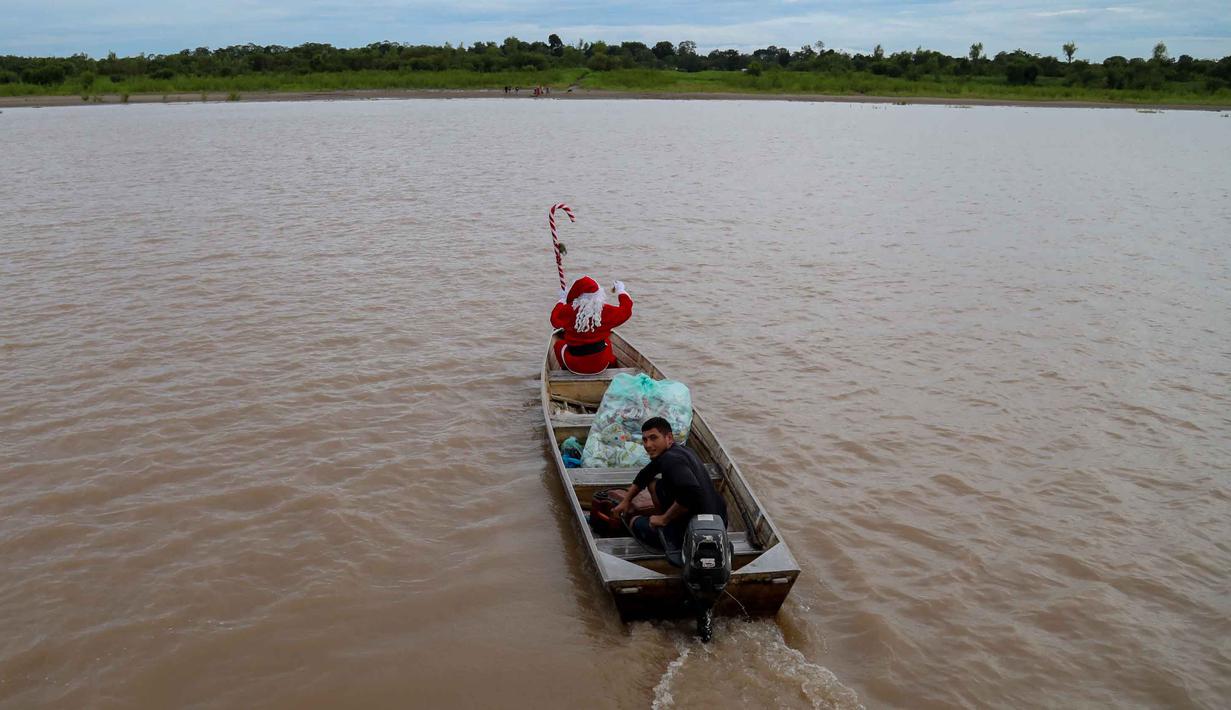 Mereka hadir untuk membawa keceriaan Natal ke wilayah-wilayah yang sulit dijangkau melalui jalur darat di pedalaman Brasil. Tampak dalam foto, relawan Jorge Alberto Barrozo, yang mengenakan kostum Sinterklas, berlayar dengan kano mengantarkan hadiah kepada anak-anak di komunitas tepi sungai di daerah pedesaan Careiro da Varzea, negara bagian Amazonas, Brasil pada Sabtu 20 Desember 2025. (Michael DANTAS/AFP)