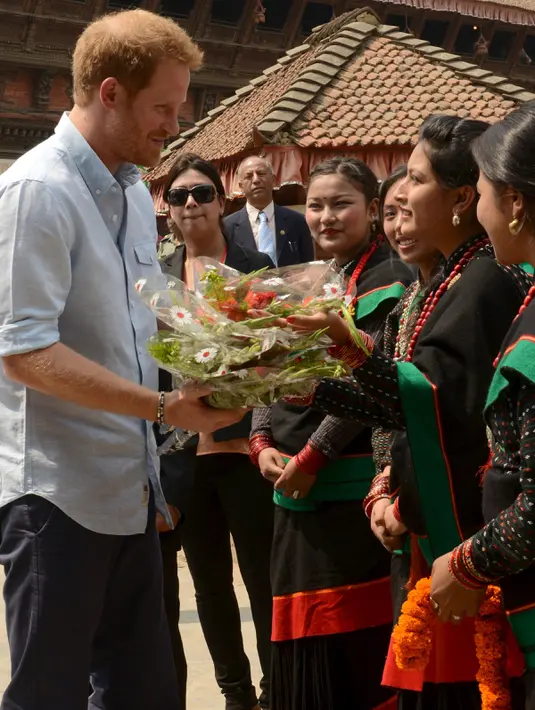 Pangeran Harry menerima buket bunga dari Panchakanya atau lima perawan khas budaya tradisional Nepal saat mengunjungi salah satu situs warisan dunia, Patan Durbar Square di Kathmandu, Minggu (20/3). (REUTERS/Prakash Mathema/Pool)
