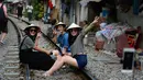 Gambar pada 21 Oktober 2018, sejumlah turis wanita duduk di atas jalur kereta api yang melintasi kawasan permukiman di Hanoi, Vietnam. Rel kereta ini menjadi titik bagi wisatawan untuk berfoto dan mengunggahnya di jejaring sosial. (Nhac NGUYEN/AFP)