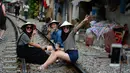Gambar pada 21 Oktober 2018, sejumlah turis wanita duduk di atas jalur kereta api yang melintasi kawasan permukiman di Hanoi, Vietnam. Rel kereta ini menjadi titik bagi wisatawan untuk berfoto dan mengunggahnya di jejaring sosial. (Nhac NGUYEN/AFP)