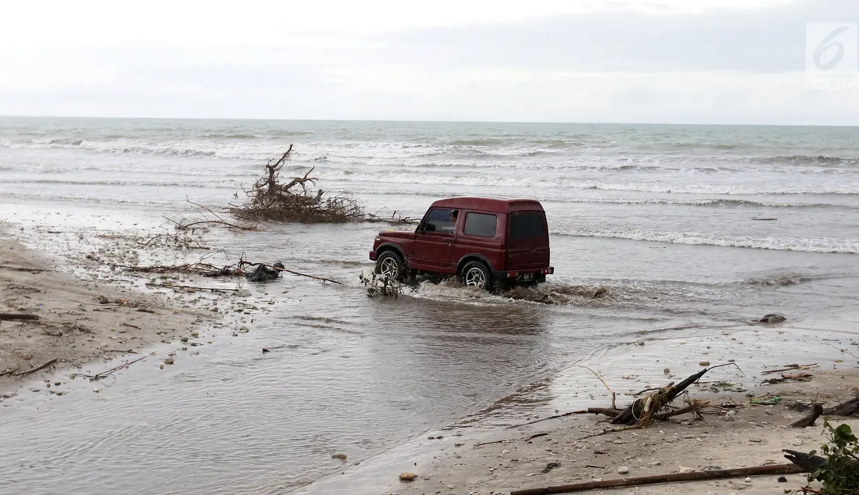 Sebuah mobil melintasi pantai karena jembatan di jalur alternatif Sumur, Banten, ambruk, Senin (24/12). Jembatan penghubung ambruk diterjang gelombang Tsunami Selat Sunda. (Liputan6.com/Angga Yuniar)