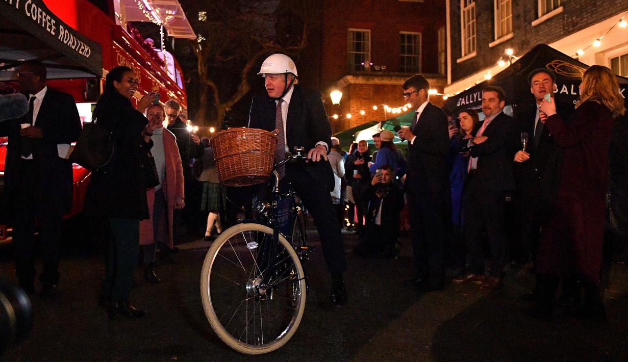 Perdana Menteri Inggris Boris Johnson mengendarai sepeda saat kunjungannya ke pasar Makanan dan Minuman Inggris yang didirikan di Downing Street, London, 30 November 2021. Sebanyak 12 bisnis dari seluruh Inggris memiliki kios untuk memamerkan produk mereka. (JUSTIN TALLIS/AFP/POOL)