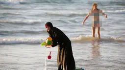 Seorang wanita muslim bermain di Pantai Laut Mediterania, Tel Aviv, Israel pada 22 Agustus 2016. Saat pengunjung pantai mengenakan busana yang minim mereka tetap mengenakan jilbab dan busananya. (REUTERS / Baz Ratner)