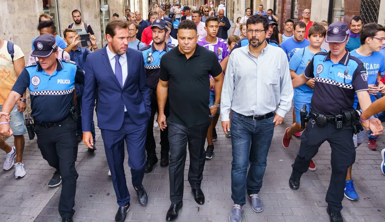 Legenda sepak bola Brasil Ronaldo berjalan bersama walikota Valladolid Oscar Puente selama tur Valladolid (3/9). Alasan Ronaldo membeli saham mayortas Valladolid untuk membangkitkan kembali klub yang sempat terdegradasi tersebut. (AFP Photo/Cesar Manso)