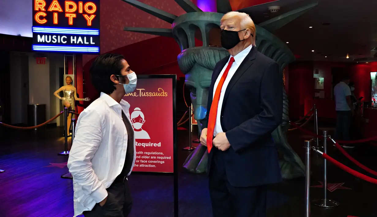 Pengunjung melihat sosok Donald Trump yang bermasker saat Madame Tussauds New York dibuka kembali di New York City, Kamis (27/8/2020). Patung lilin Donald Trump akan berada di pintu masuk untuk mengingatkan pengunjung tentang protokol kesehatan, termasuk pemakaian masker (Cindy Ord/Getty Images/AFP)
