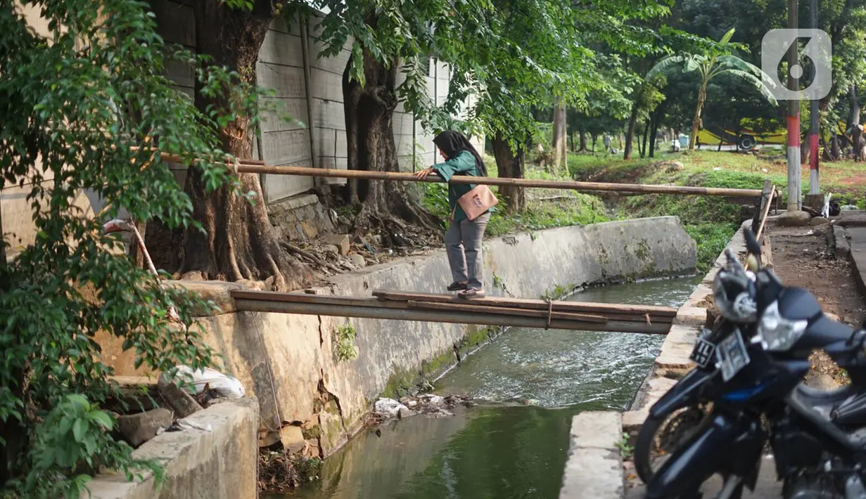 Pejalan kaki melintasi jembatan saat akan melewati tembok berlubang di Terminal Kampung Rambutan, Jakarta, Kamis (19/12/2019). Jauhnya akses bagi pejalan kaki menjadikan tembok berlubang tersebut pintu alternatif untuk keluar dan masuk Terminal Kampung Rambutan. (Liputan6.com/Immanuel Antonius)