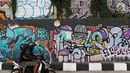 Pengendara melintasi jalur inspeksi Sungai Ciliwung di Jakarta, Kamis (27/12). Mural yang dibuat oleh beberapa komunitas tersebut menjadikan jalur inspeksi Sungai Ciliwung tampak lebih berwarna dan asri. (Liputan6.com/Immanuel Antonius)
