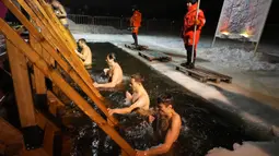 Petugas penyelamat mengamati penganut Kristen Ortodoks Rusia berendam dalam air es saat perayaan Epiphany tradisional di St. Petersburg, Rusia, 19 Januari 2022. Ribuan penganut Kristen Ortodoks Rusia merayakan Epiphany dengan membenamkan diri dalam air dingin. (AP Photo/Dmitri Lovetsky)