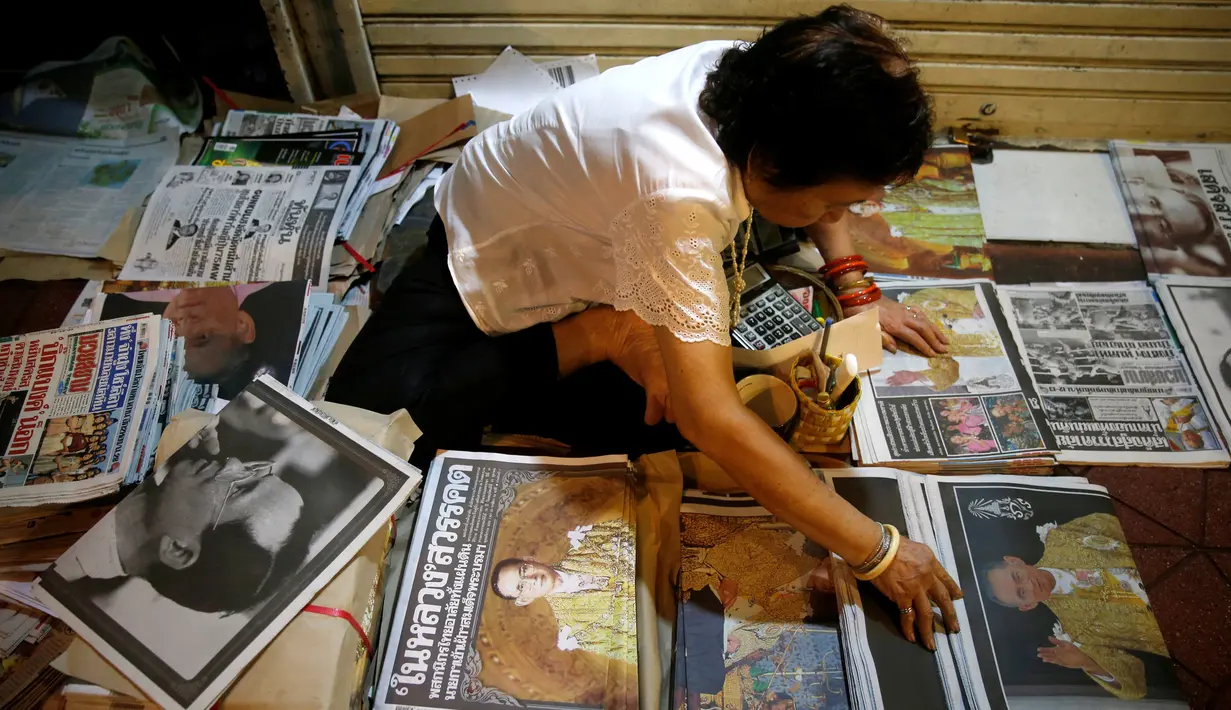 Seorang pedagang merapikan koran-koran jualannya yang memberitakan wafatnya Raja Thailand Bhumibol Adulyadej, di Bangkok, Jumat (14/10). Raja Bhumibol meninggal di usia 88 tahun dan wajahnya menghiasi berbagai media cetak di Thailand. (Reuters/Edgar Su)