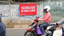 Pengendara motor melintas di depan poster protes warga terhadap pembangunan flyover di kawasan Tanjung Barat, Jakarta, Rabu (15/7/2020). Dalam poster protes tersebut, warga menuntut agar pembayaran pelunasan pembebasan lahan segera diselesaikan secara serentak. (Liputan6.com/Immanuel Antonius)