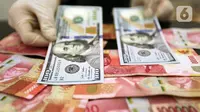 Karyawan menunjukkan uang dolar AS dan rupiah di Jakarta, Rabu (30/12/2020). Nilai tukar rupiah di pasar spot ditutup menguat 80 poin atau 0,57 persen ke level Rp 14.050 per dolar AS. (Liputan6.com/Johan Tallo)