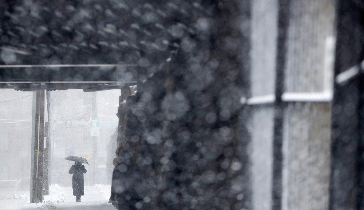 Seorang wanita menggunakan payung berjalan di bawah salju lebat saat terjadi badai salju di Hoboken, New Jersey (21/3). Karena badai salju yang melanda New Jersey ini layanan komuter dan bus dihentikan pada pukul 3 sore. (AP/Julio Cortez)