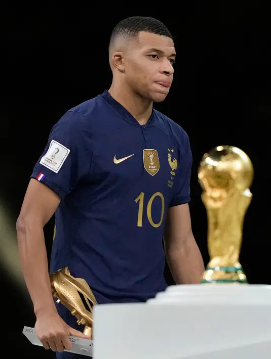 <p>Pemain Prancis Kylian Mbappe berjalan melewati trofi juara dengan membawa trofi penghargaan Sepatu Emas usai melawan Argentina pada pertandingan sepak bola final Piala Dunia 2022 di Stadion Lusail, Lusail, Qatar, 18 Desember 2022. Kylian Mbappe berhak membawa pulang trofi penghargaan Sepatu Emas setelah menjadi pencetak gol terbanyak selama gelaran Piala Dunia 2022. (AP Photo/Martin Meissner)</p>