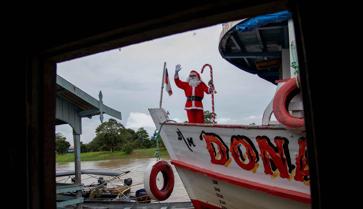 Menyusuri tepi sungai hutan hujan Amazon, para relawan berharap kebahagiaan Natal bisa dirasakan anak-anak di wilayah tersebut. Tampak dalam foto, relawan Jorge Alberto Barrozo, yang mengenakan kostum Sinterklas, berlayar dengan kano mengantarkan hadiah kepada anak-anak di komunitas tepi sungai di daerah pedesaan Careiro da Varzea, negara bagian Amazonas, Brasil pada Sabtu 20 Desember 2025. (Michael DANTAS/AFP)