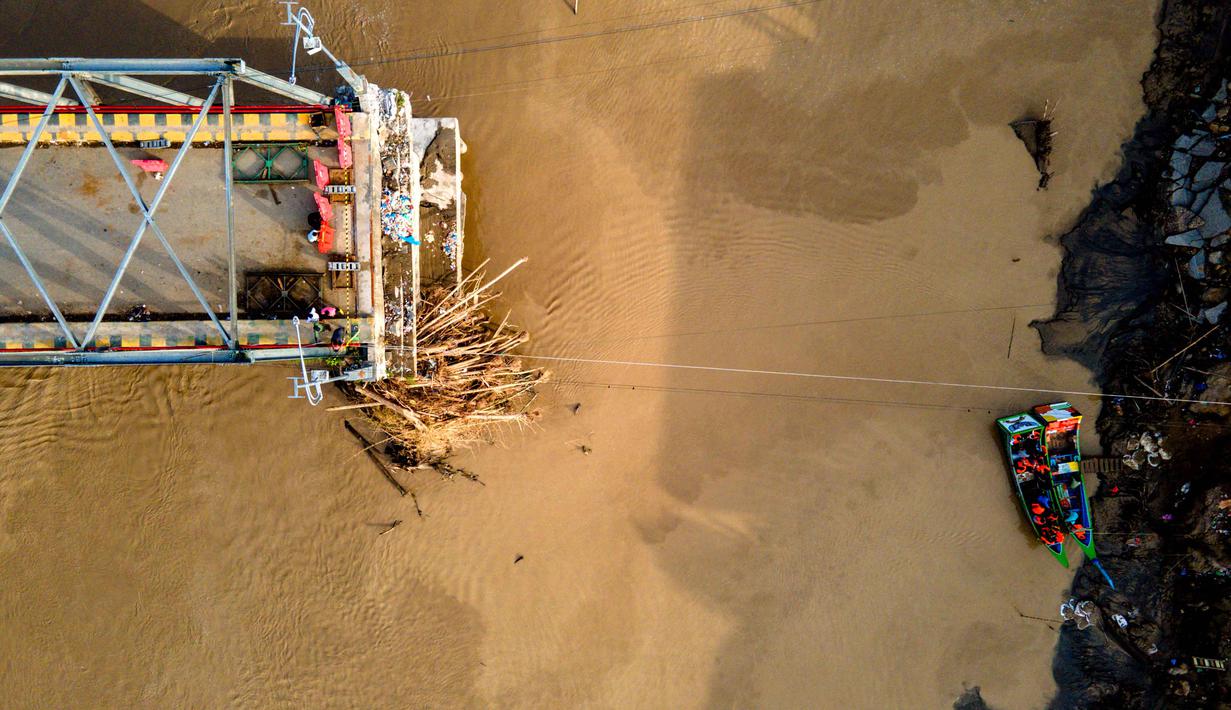 Diketahui, jembatan ini merupakan akses vital dari Jalan Lintas Sumatera (Jalinsum) yang menjadi penghubung utama antara Banda Aceh dan Medan, Sumatera Utara. Tampak foto udara menunjukkan perahu-perahu (kanan) yang mengangkut penumpang menyeberangi Sungai Peusangan di Kuta Blang, Kabupaten Bireuen, Provinsi Aceh, Selasa 9 Desember 2025. (CHAIDEER MAHYUDDIN/AFP)