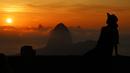 Seorang wisatawan berpose saat matahari terbit dengan latar belakang gunung Sugarloaf di Bukit Corcovado di Rio de Janeiro, Brasil, pada 24 Maret 2023. (Photo by Carl DE SOUZA / AFP)