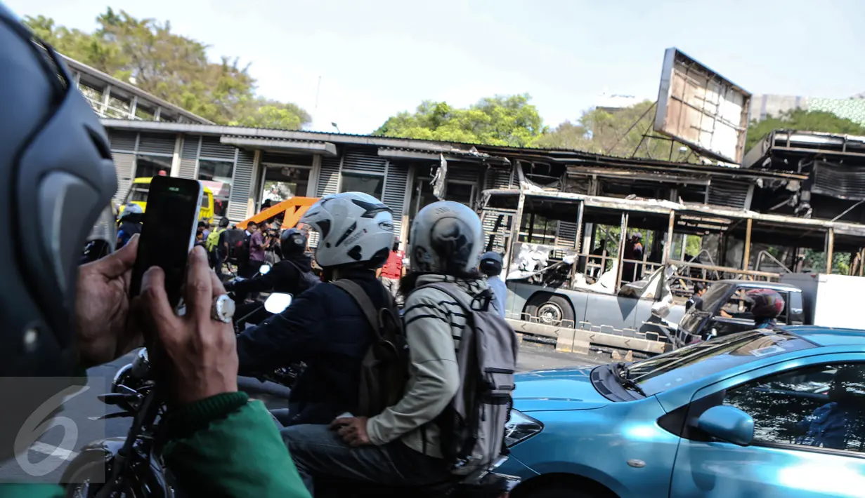 Pengendara yang melintas mengabadikan gambar bangkai Bus Transjakarta yang terbakar di Halte UI Salemba, Jakarta, Jumat (3/7). Bus Koridor V jurusan Ancol-Kampung Melayu tersebut terbakar sekitar pukul 08.30 WIB. (Liputan6.com/Faizal Fanani)
